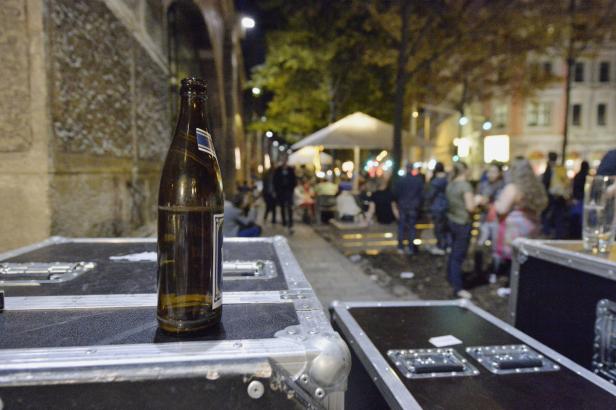 Eine leere Bierflasche steht auf einem Flightcase im abendlichen Außenbereich.