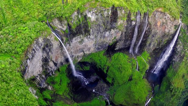 Mehrere Wasserfälle stürzen von einer grünen Klippe herab.