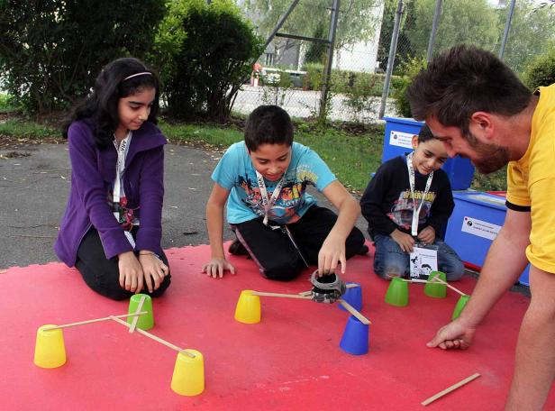 Kinder und ein Mann bauen gemeinsam eine Konstruktion mit Bechern und Holzstäben.
