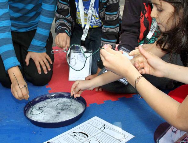Kinder sitzen auf dem Boden und machen Seifenblasen mit Drahtformen.