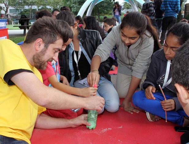 Eine Gruppe von Kindern und ein Mann experimentieren mit einer Plastikflasche auf einer roten Oberfläche.