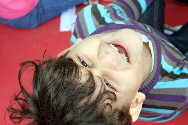 Ein lachender Junge mit braunen Haaren liegt auf dem Rücken.