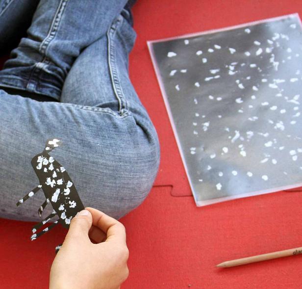 Eine Person bastelt mit Papier und Farbe auf einem roten Untergrund.