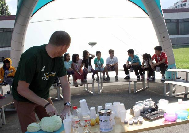 Ein Mann schneidet Kohl vor einer Gruppe von Kindern, die auf Bänken sitzen.