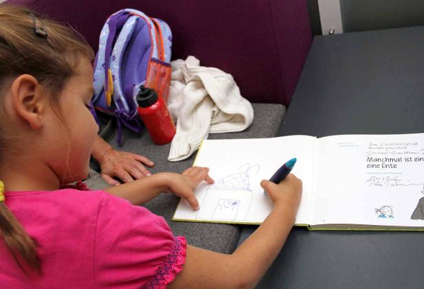 Ein Mädchen zeichnet mit einem blauen Stift ein Haus in ein Buch.