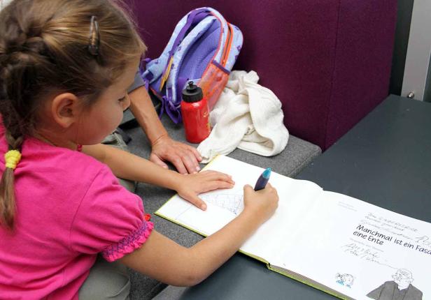 Ein junges Mädchen zeichnet in einem Buch, daneben eine erwachsene Person.