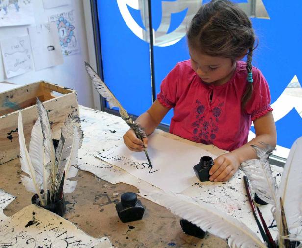 Ein Mädchen schreibt mit einer Feder und Tinte auf ein Blatt Papier.