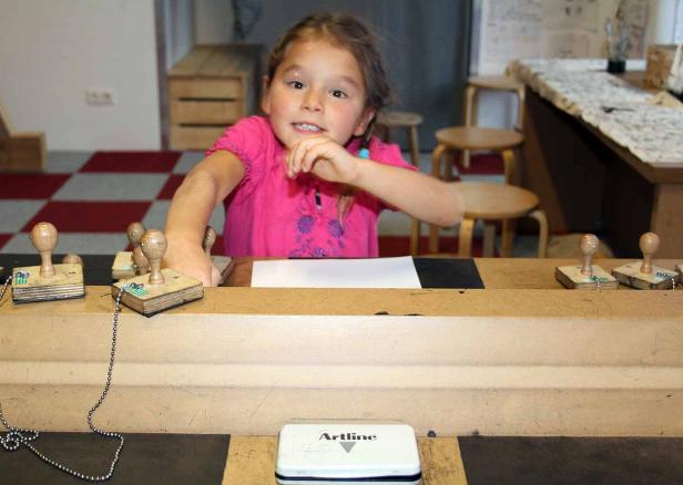 Ein Mädchen stempelt mit verschiedenen Holzstempeln auf ein Blatt Papier.