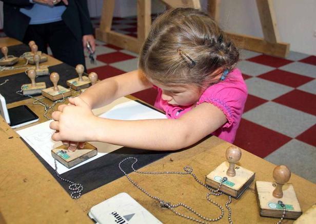 Ein Mädchen stempelt mit Holzstempeln auf ein Blatt Papier.