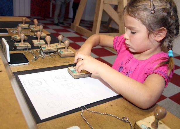Ein Mädchen stempelt Buchstaben auf ein Blatt Papier.