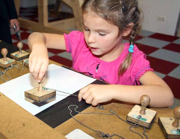 Ein Mädchen stempelt mit Holzstempeln auf ein Blatt Papier.