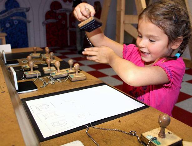 Ein Mädchen stempelt Buchstaben auf ein Blatt Papier.