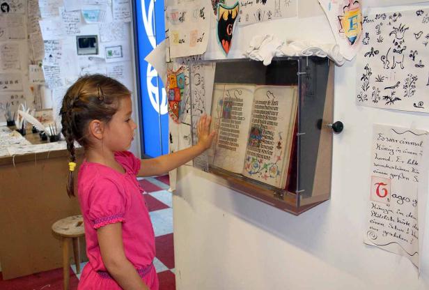 Ein Mädchen betrachtet ein altes Buch in einer Vitrine.