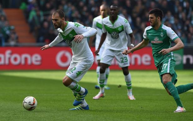 Ein Fußballspieler des VfL Wolfsburg dribbelt den Ball, während ein Spieler von Werder Bremen ihn verfolgt.