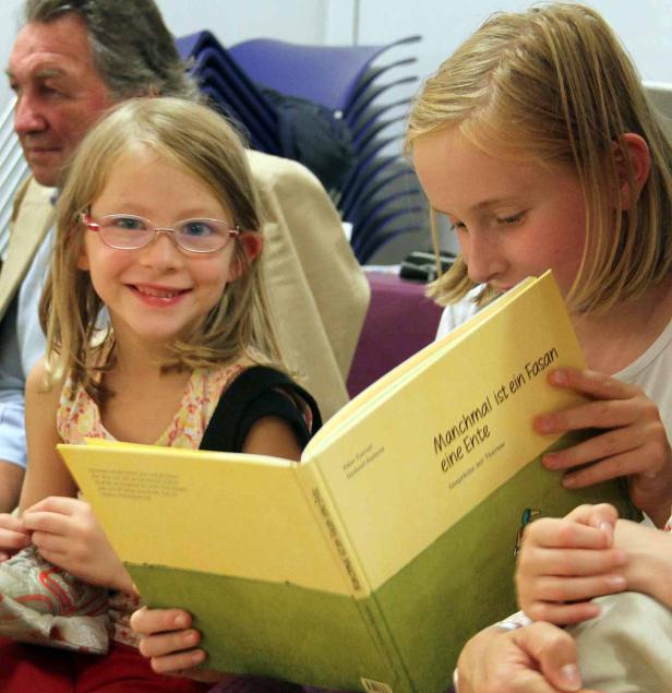Zwei Mädchen lesen gemeinsam ein Buch mit dem Titel „Manchmal ist ein Fasan eine Ente“.