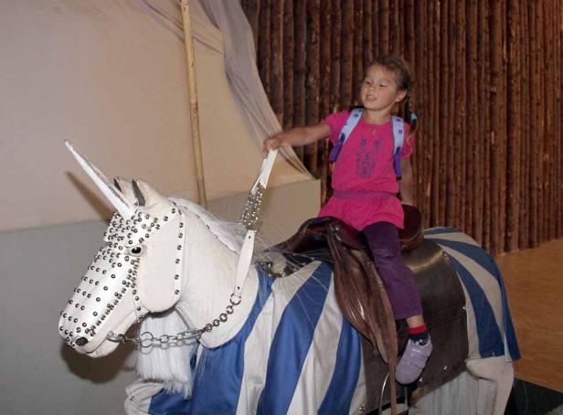 Ein kleines Mädchen reitet auf einem geschmückten Spielzeug-Einhorn.