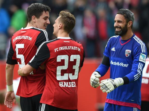 Zwei Fußballspieler von FC Ingolstadt 04 umarmen sich, während der Torwart daneben steht.