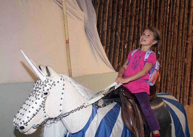 Ein Mädchen mit Rucksack reitet auf einem geschmückten Spielzeug-Einhorn.