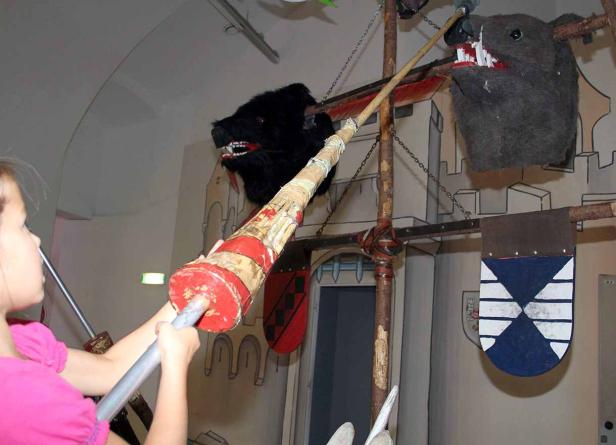 Ein Mädchen versucht, mit einer Lanze auf zwei Wildschweinköpfe zu zielen.