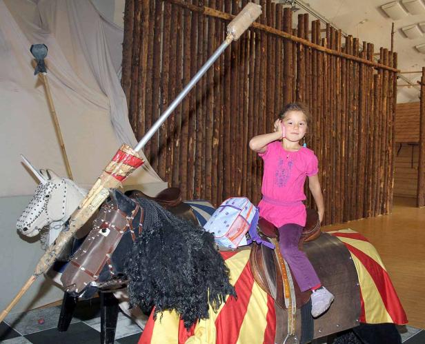 Ein junges Mädchen reitet auf einem Spielzeugpferd mit Lanze.