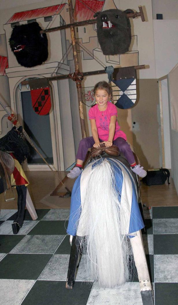 Ein Mädchen reitet auf einem Steckenpferd in einer mittelalterlichen Kulisse.