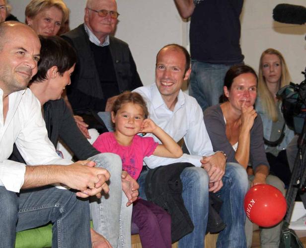 Eine Gruppe von Menschen sitzt zusammen, darunter ein junges Mädchen mit einem roten Ballon.