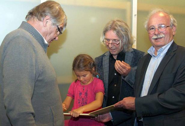 Ein junges Mädchen unterschreibt ein Buch, umgeben von drei älteren Männern.