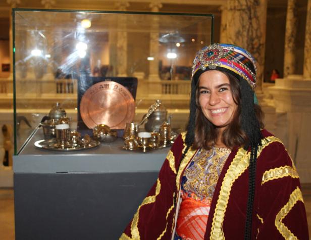 Eine Frau in traditioneller Kleidung steht vor einer Vitrine mit Tee-Service.