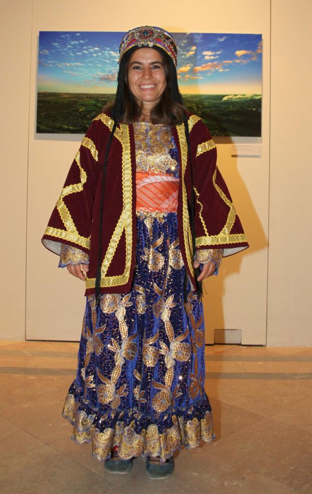 Eine Frau in traditioneller kurdischer Kleidung steht vor einem Landschaftsbild.