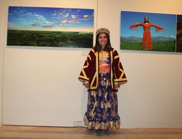 Eine Frau in traditioneller Kleidung steht vor zwei Landschaftsbildern.