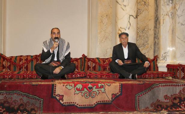 Zwei Männer sitzen auf einem traditionellen Sofa und sprechen in ein Mikrofon.