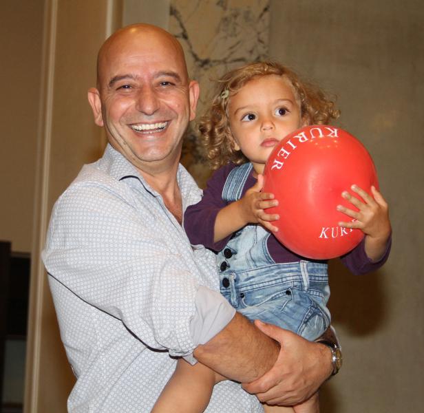 Ein lächelnder Mann hält ein kleines Mädchen mit einem roten „Kurier“-Ballon im Arm.