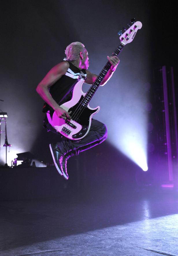 Ein Bassist springt mit seiner Gitarre auf der Bühne.