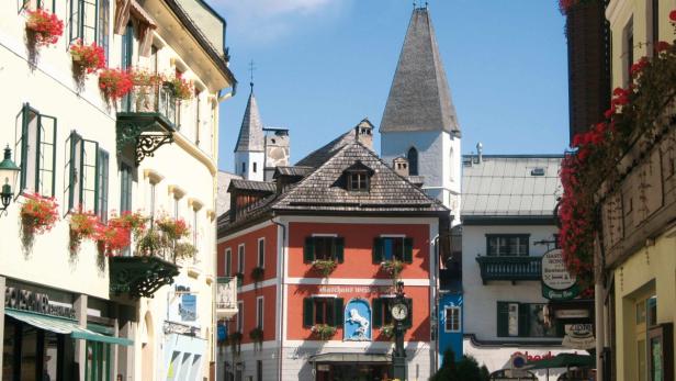 Blick auf eine malerische Gasse mit blumengeschmückten Häusern und Kirchtürmen in Österreich.