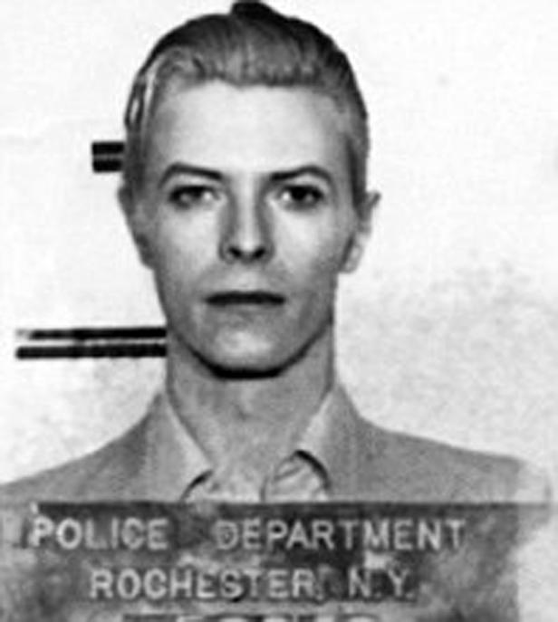 Schwarzweiß-Porträt von David Bowie vor einer Tafel der Polizei von Rochester, N.Y..