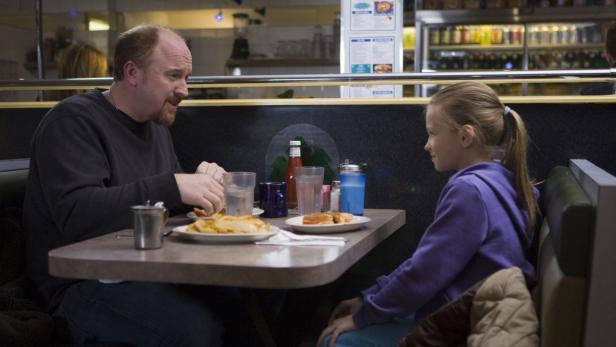 Ein Mann und ein junges Mädchen sitzen in einem Diner und essen Pommes und Sandwiches.