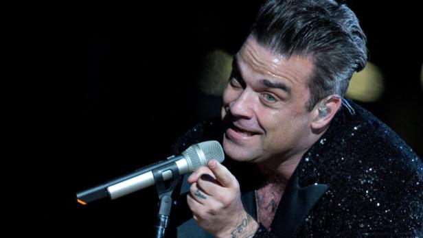 Robbie Williams singt in einem glitzernden Sakko ins Mikrofon.