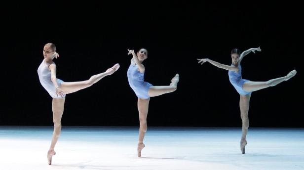 Drei Ballerinen in blauen Trikots tanzen auf einer Bühne.