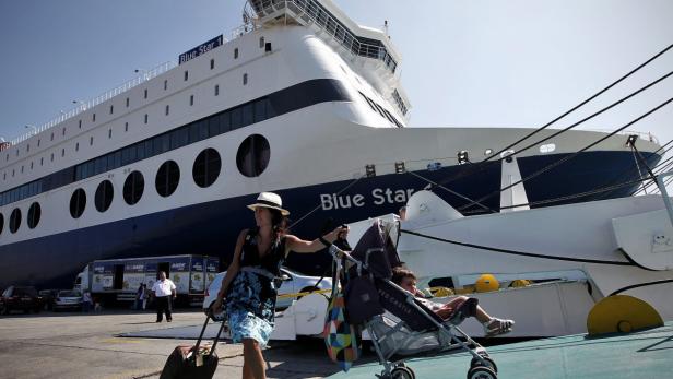 GREECE TOURISM Eine Frau zieht einen Koffer und schiebt einen Kinderwagen vor einem „Blue Star“-Fährschiff.
