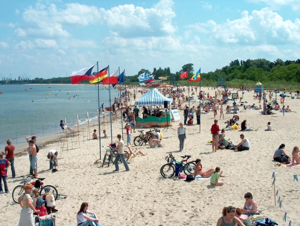 Ein belebter Strand mit vielen Menschen, Fahrrädern und verschiedenen Flaggen.