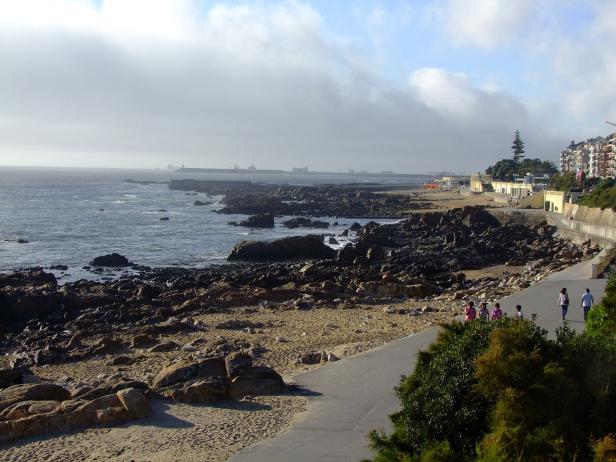 Eine Küstenlandschaft mit Felsen, einem Strand und einer Promenade mit Spaziergängern.