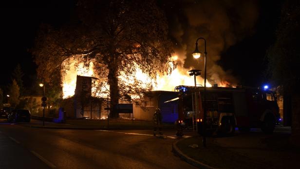 Ein Gebäude steht in Flammen, während ein Feuerwehrmann und ein Feuerwehrauto daneben stehen.