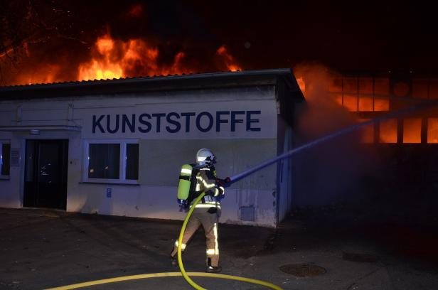 Ein Feuerwehrmann bekämpft einen Brand in einem Gebäude mit der Aufschrift „Kunststoffe“.