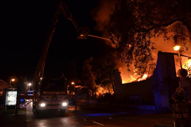 Ein Feuerwehrauto löscht ein brennendes Gebäude in der Nacht.