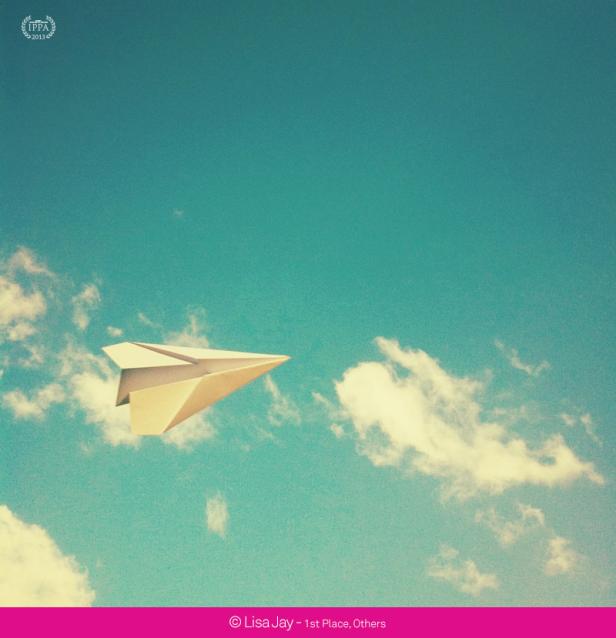 Ein Papierflieger fliegt vor blauem Himmel mit Wolken.