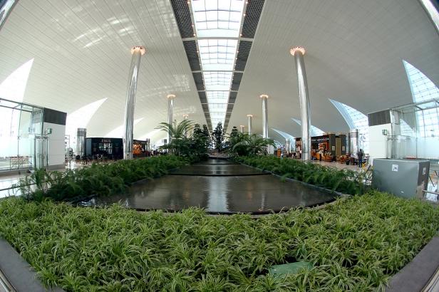 Ein Brunnen mit tropischen Pflanzen in einem hellen, modernen Flughafenterminal.