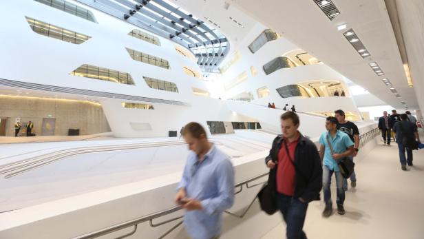 Menschen gehen durch das Innere des futuristischen Gebäudes der Wirtschaftsuniversität Wien.