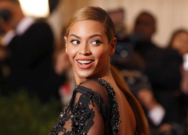 Beyoncé lächelt in einem schwarzen, verzierten Kleid über die Schulter.