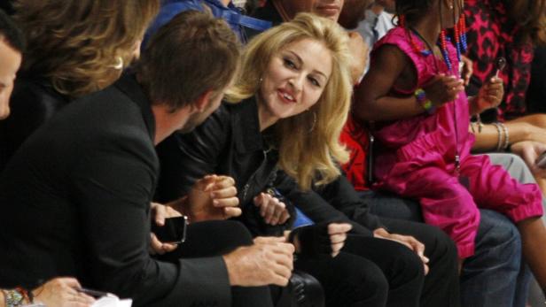Madonna sitzt bei einer Veranstaltung neben anderen Gästen.