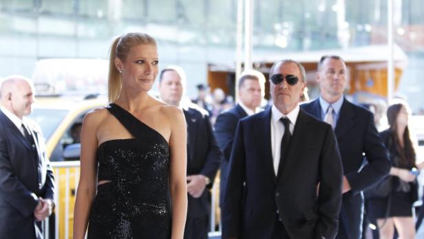 Gwyneth Paltrow in einem schwarzen Kleid, umgeben von Bodyguards.